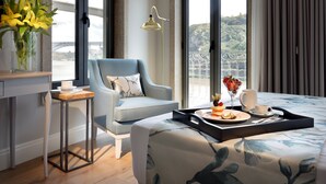 A modern hotel room with a bed, a desk, a chair, a vase of flowers, and a tray with breakfast items. - Eurostars Porto Douro (Porto)