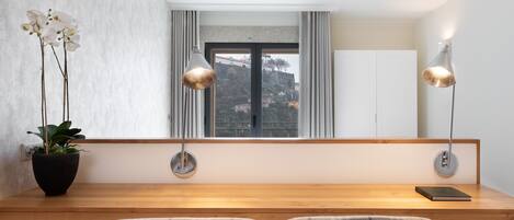 Una habitación moderna con un escritorio de madera, dos sillas a cuadros, una planta en maceta y vistas a un paisaje urbano a través de una ventana.