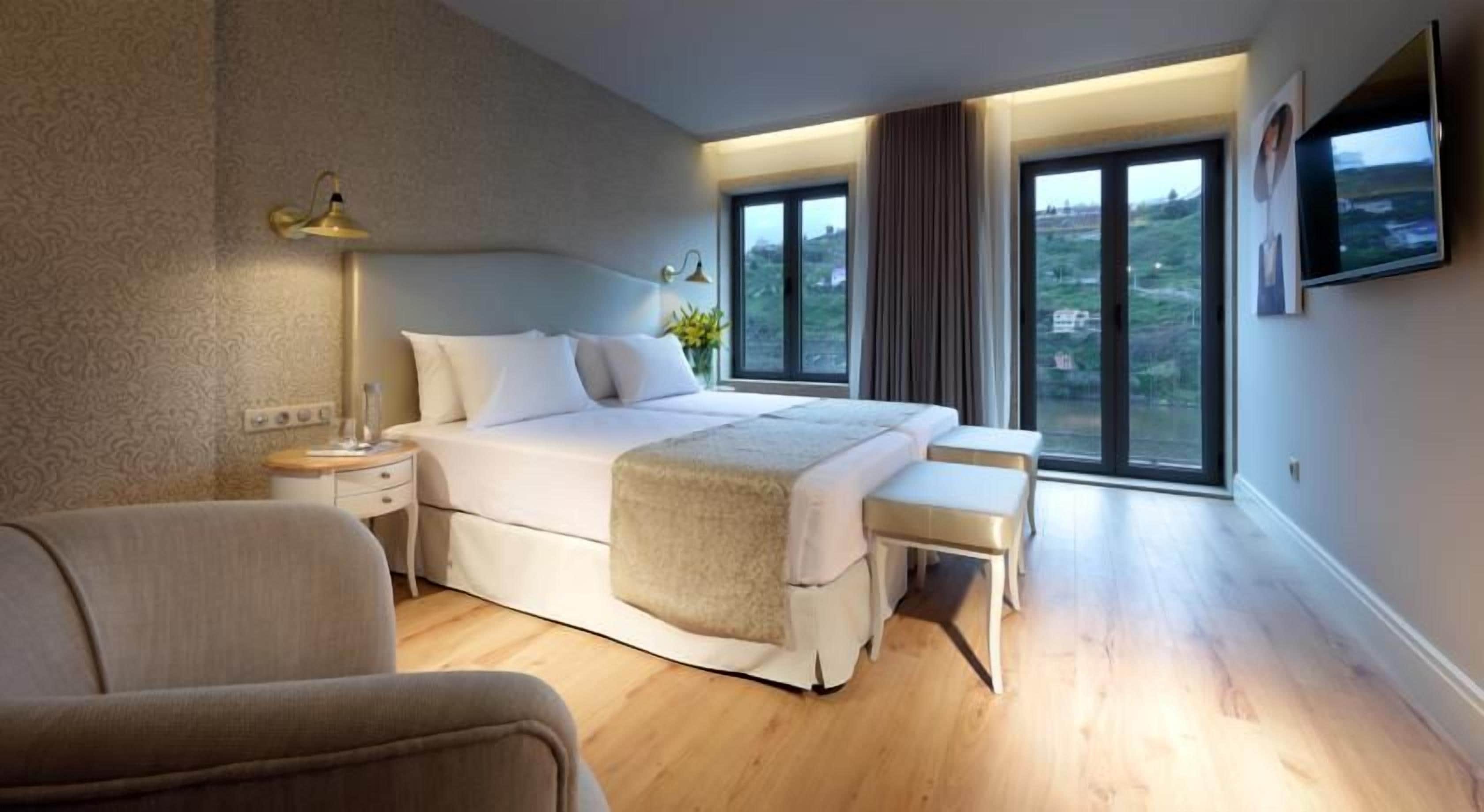 Quarto moderno com uma cama grande, mesas de cabeceira, um banco e uma TV na parede.