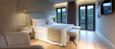 A modern bedroom with a large bed, bedside tables, a bench, and a TV on the wall.