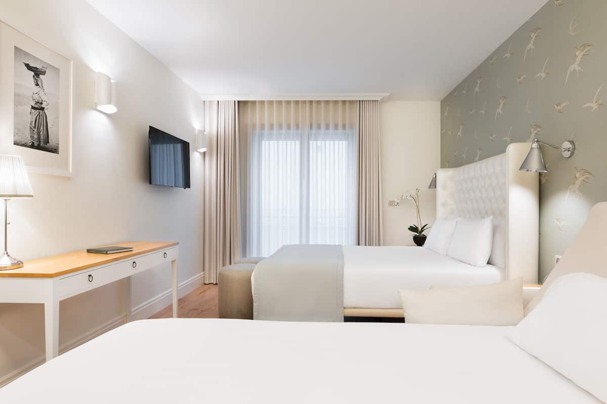 A hotel room with a bed, a desk, a chair, a TV, and a window with curtains.
