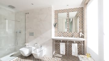 A modern bathroom with a glass shower enclosure, a bidet, a sink, and a vanity with a patterned tile backsplash.