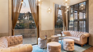 A luxurious room with a large window, a plush sofa, a round ottoman, and a small table. - Eurostars Porto Douro (Porto)