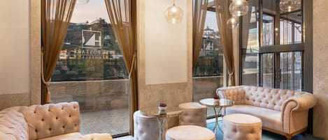A luxurious room with a large window, a plush sofa, a round ottoman, and a small table.