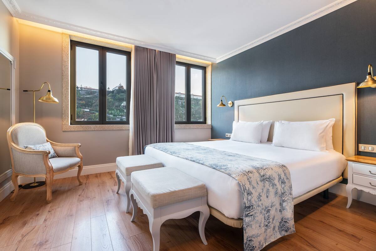 A bedroom with a large bed, a chair, a bench, and a nightstand.