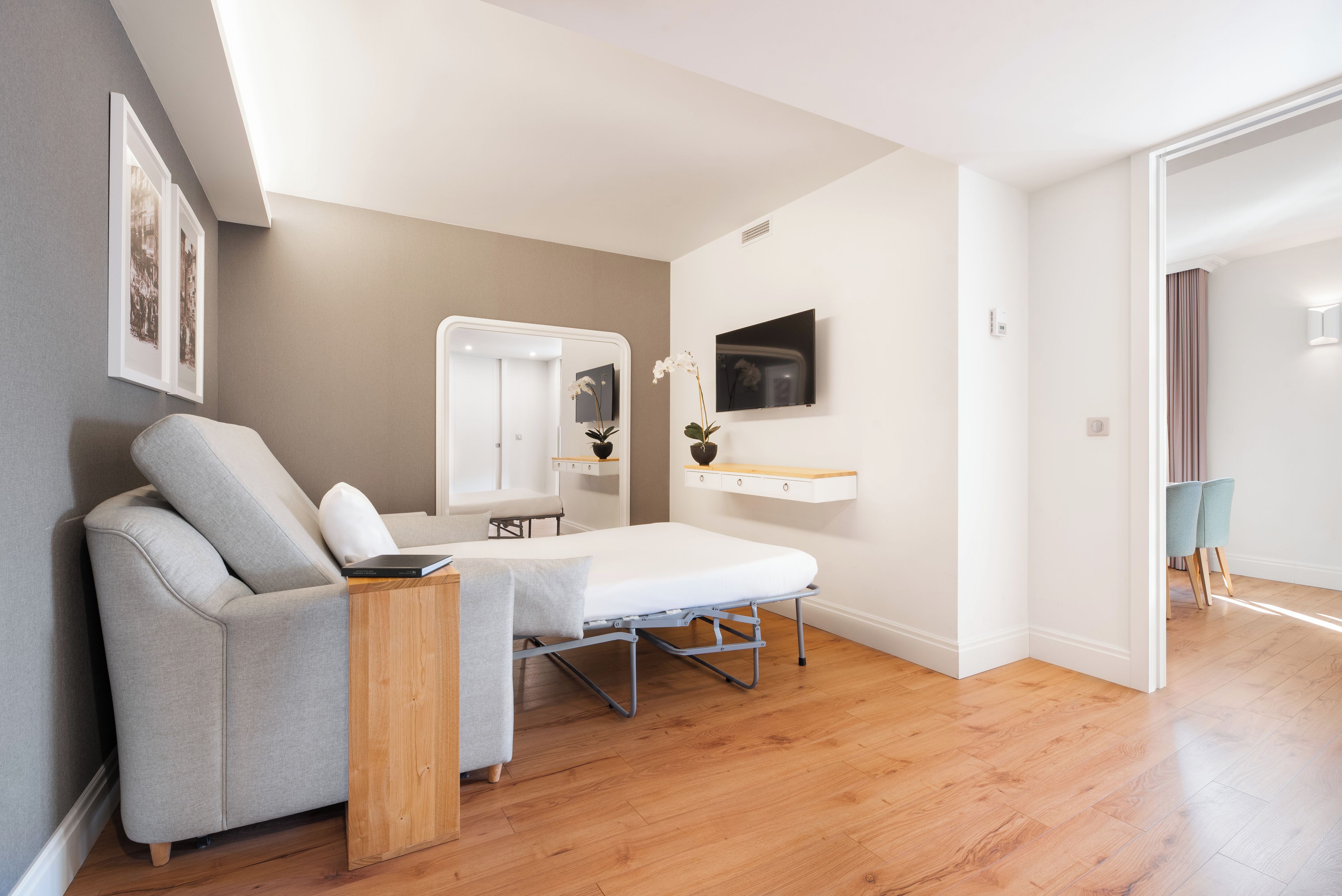 A modern bedroom with a bed, a bedside table, a chair, a TV, and a mirror.