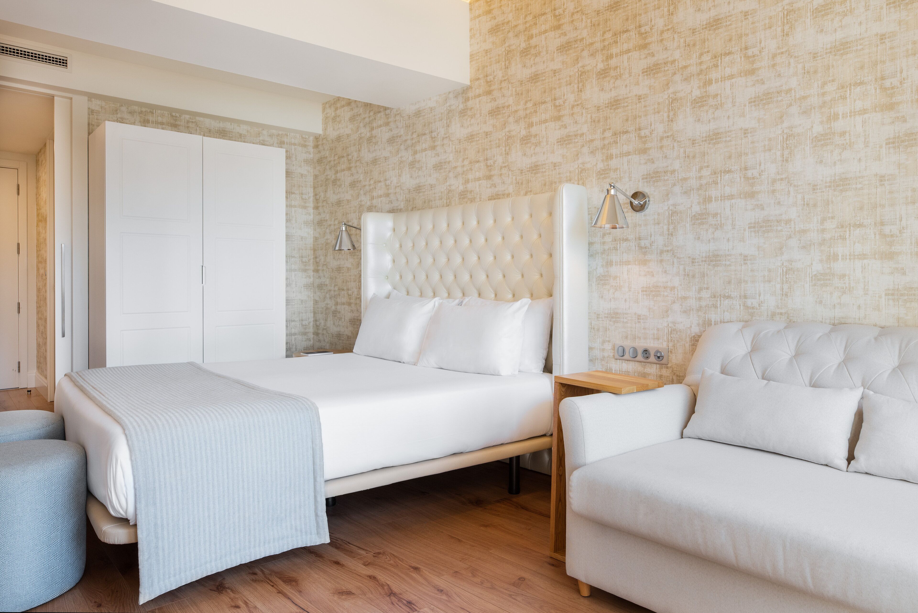 A modern bedroom with a large bed, a sofa, and a wardrobe.