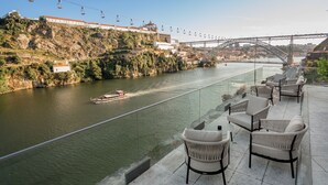 A riverside terrace with wicker chairs and a view of a bridge and river. - Eurostars Porto Douro (Porto)