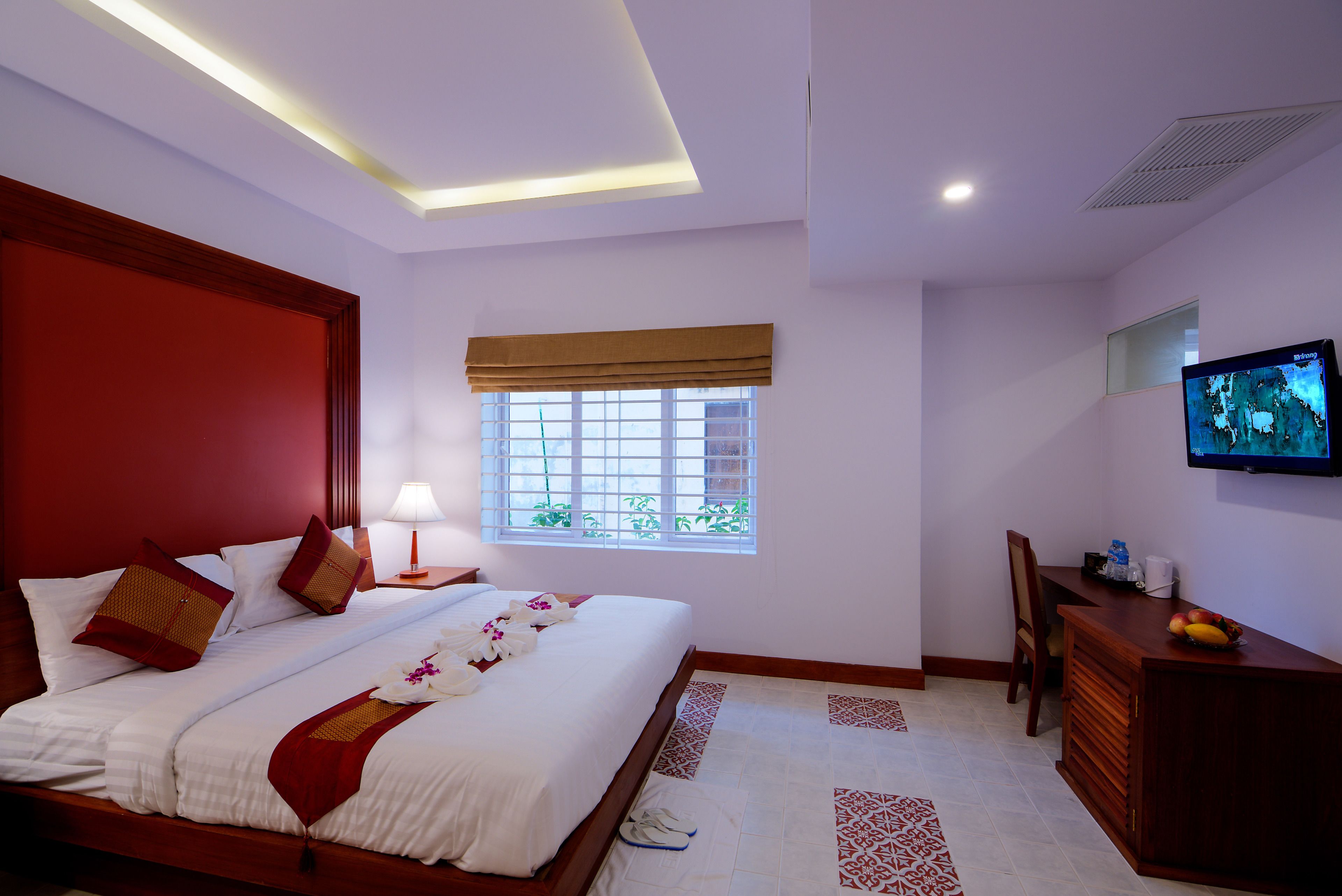 A hotel room with a large bed, a desk, a television, and a window with a view of greenery.