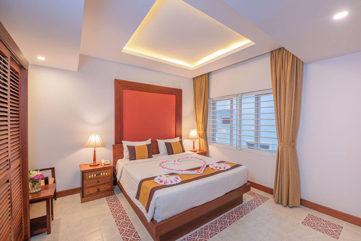 A hotel room with a large bed, bedside lamps, a window with curtains, and a wooden headboard.