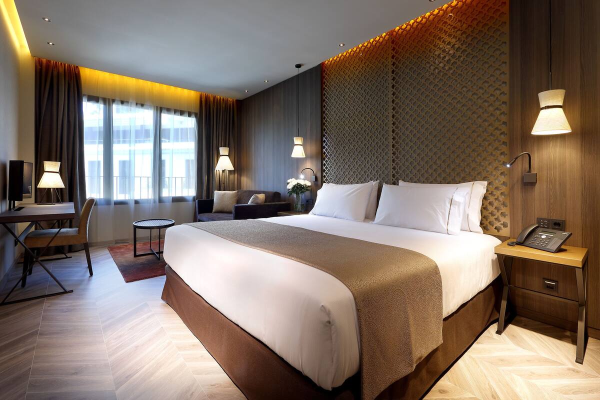 Ein Hotelzimmer mit einem großen Bett, einem Schreibtisch, einem Sessel, einem kleinen Tisch und einer Lampe.