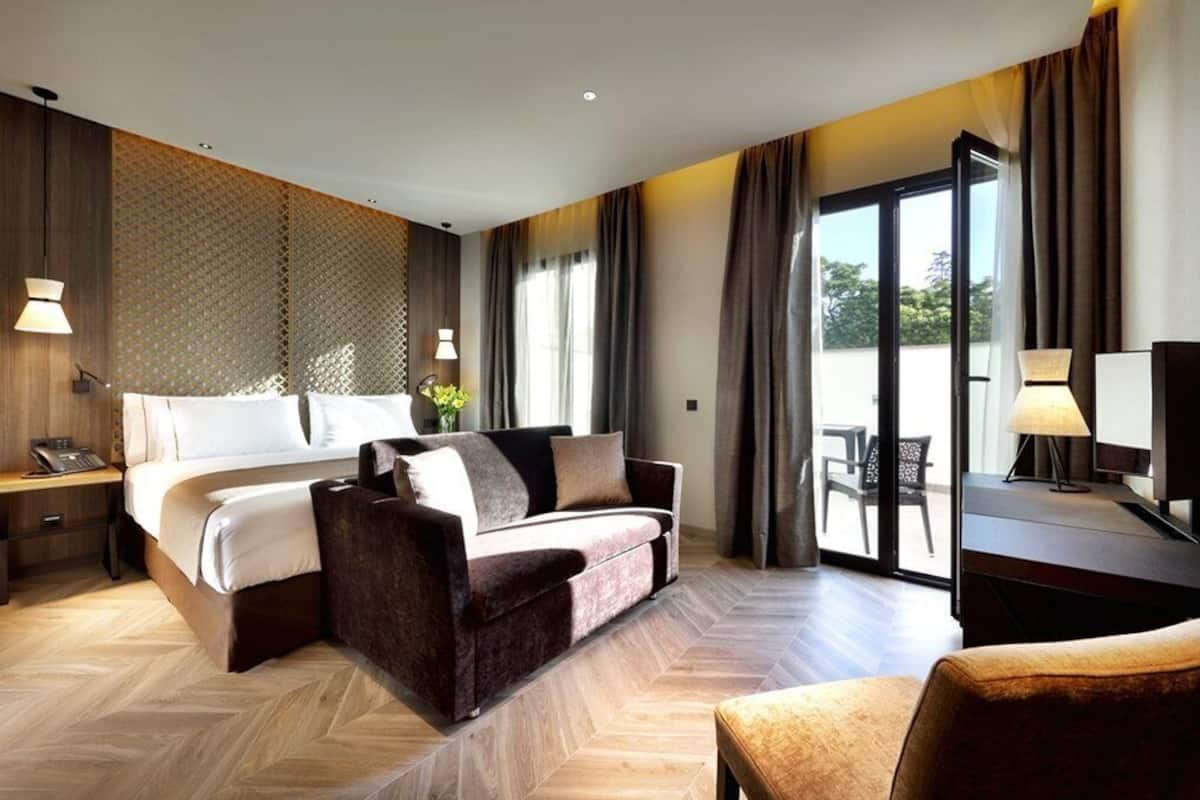 Ein modernes Hotelzimmer mit einem großen Bett, einer Couch, einem Schreibtisch und einem Balkon mit Tisch und Stühlen.
