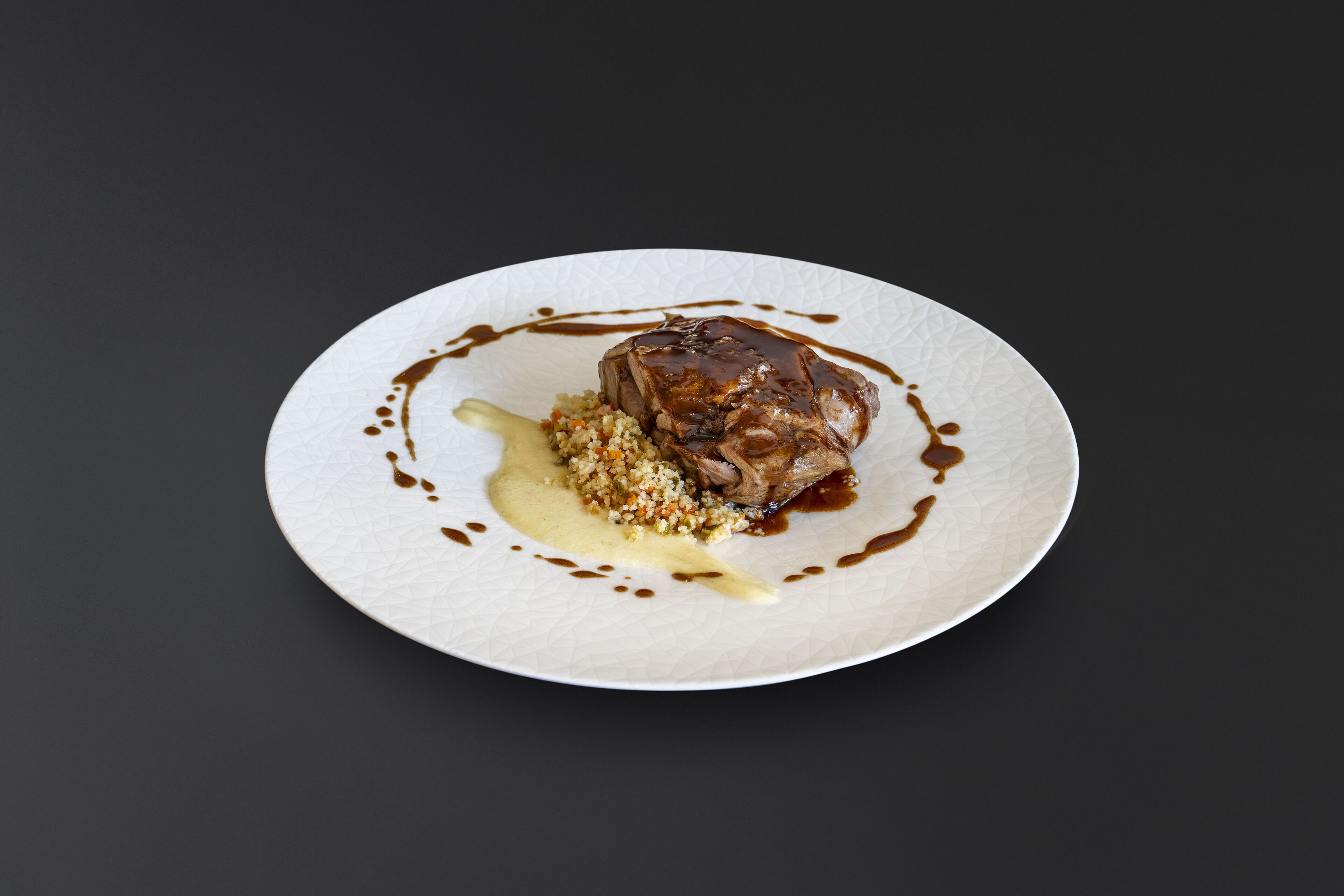 Une assiette comprenant un morceau de viande, un accompagnement de couscous et une sauce.