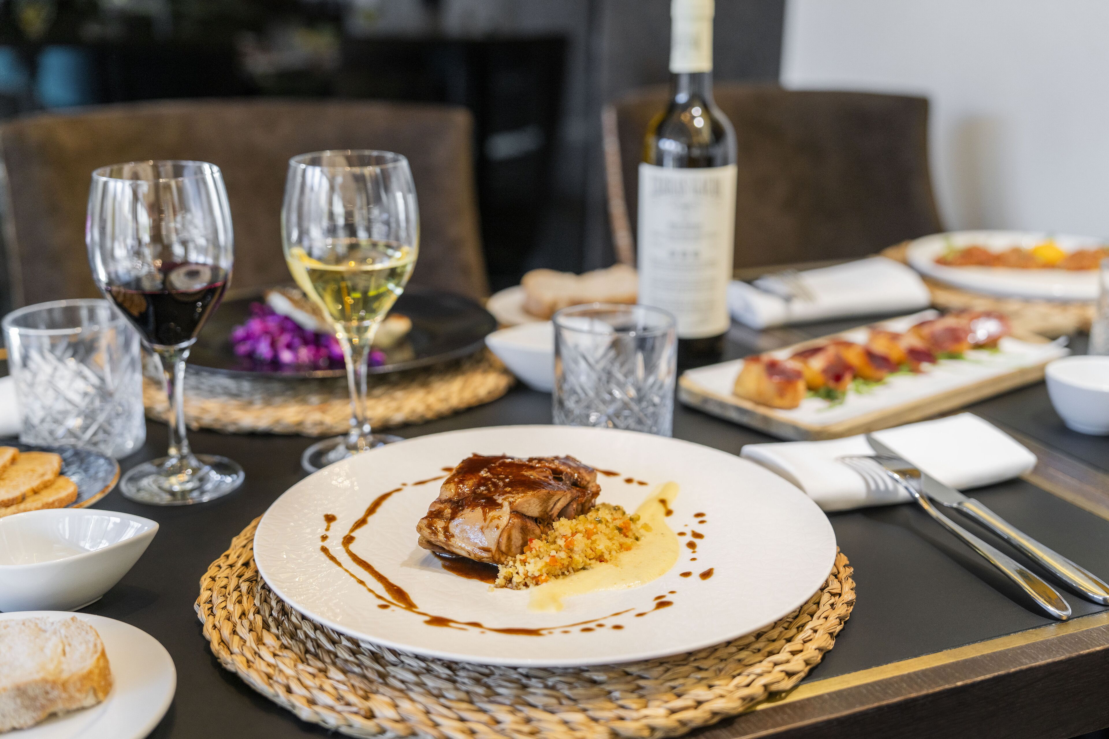 A dining table set with plates of food, wine glasses, and a bottle of wine.