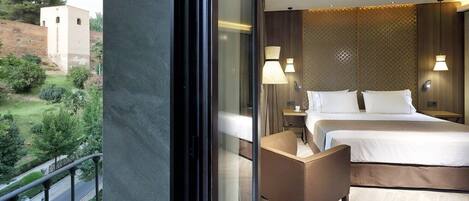 A hotel room with a large bed, two bedside tables, and a view of a garden and building outside.