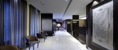 A hotel corridor with seating areas, a reception desk, and a large informational poster on the wall.