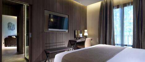 A modern hotel room with a large bed, a desk, a flat-screen TV, and a view of the outdoors through the window.
