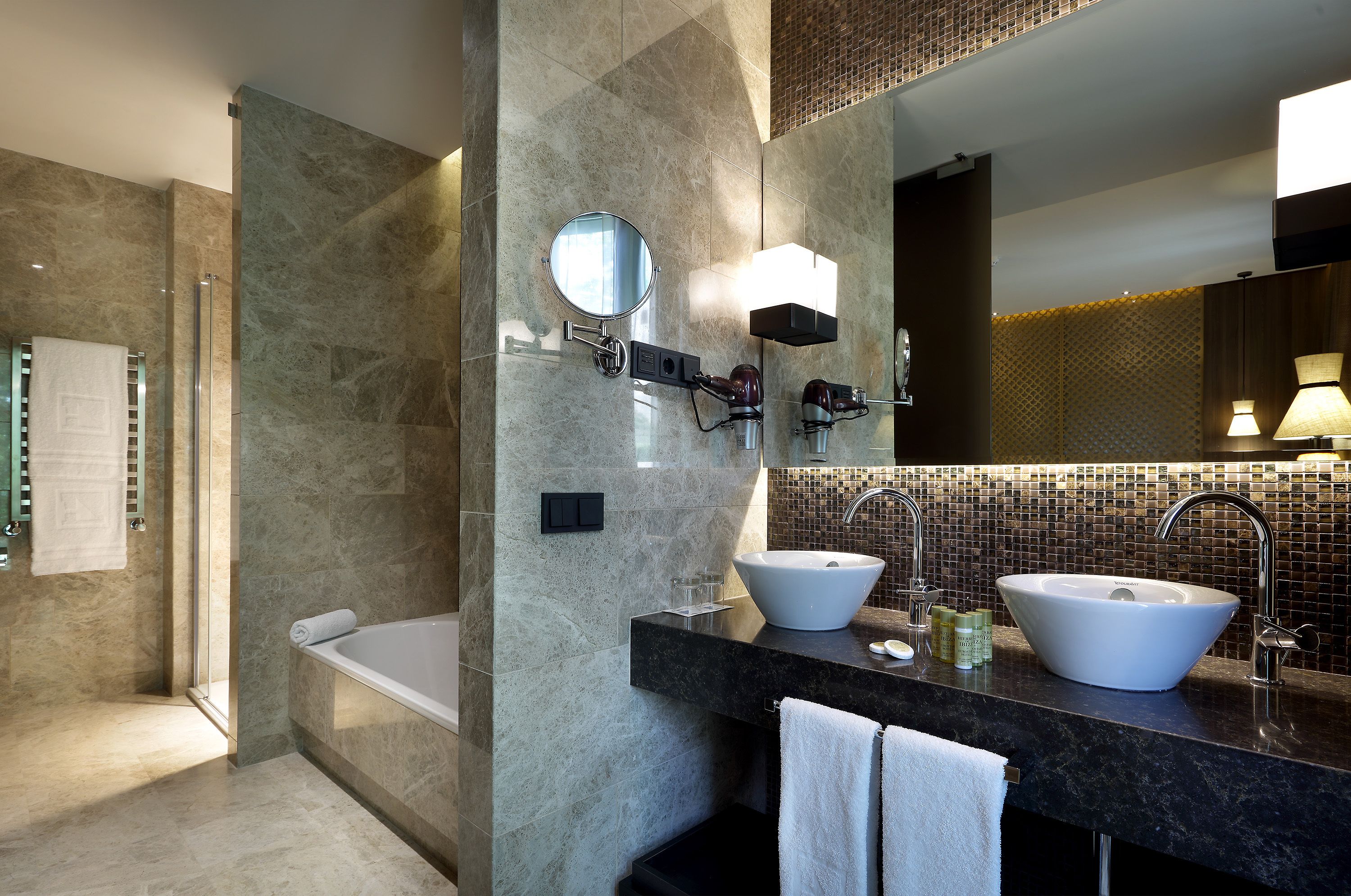 A modern bathroom with a bathtub, two sinks, a large mirror, and a shower area.