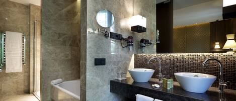 A modern bathroom with a bathtub, two sinks, a large mirror, and a shower area.