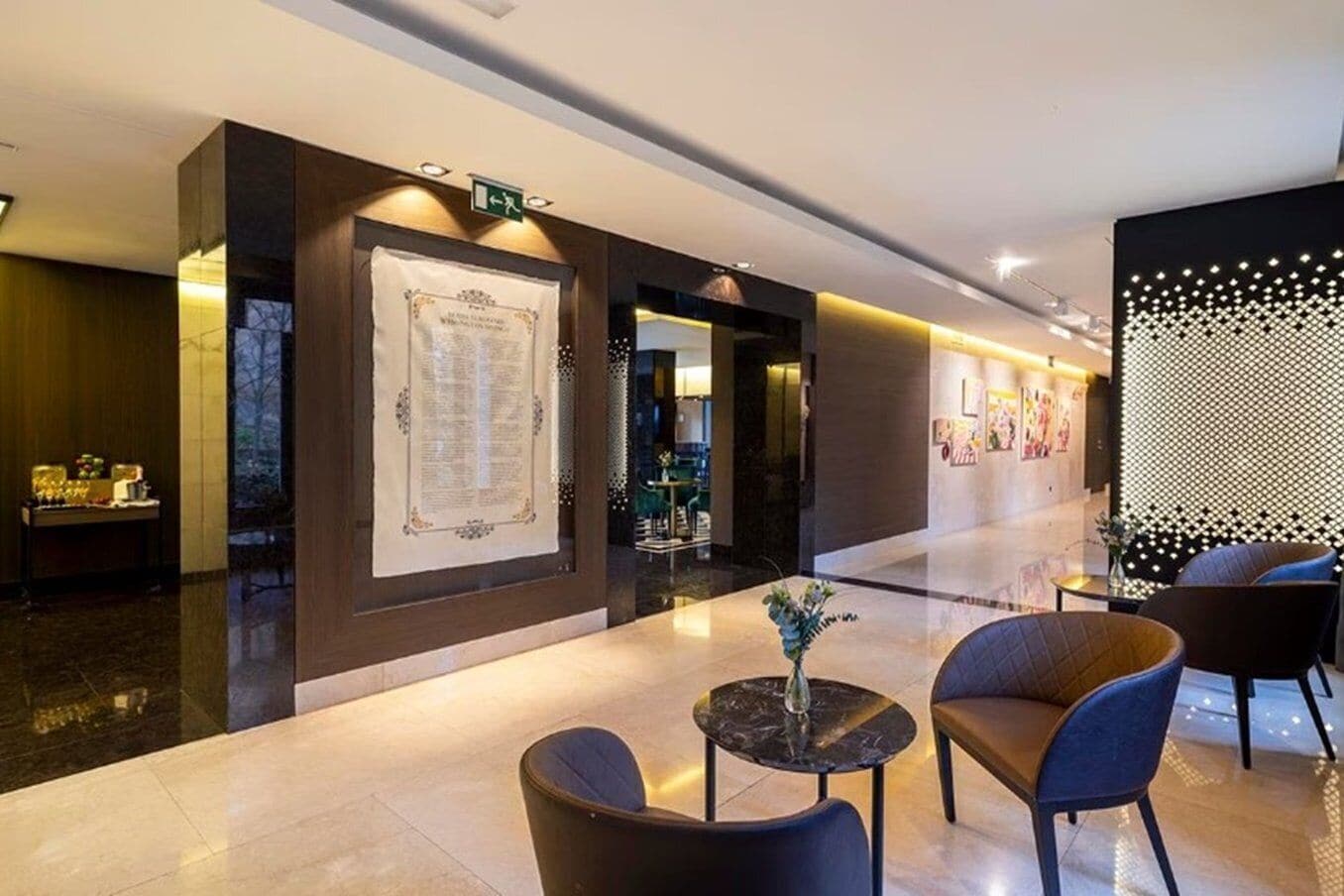 A modern hotel lobby with a reception desk, seating area, and a decorative wall with a geometric pattern.