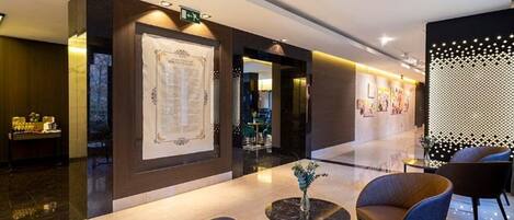 A modern hotel lobby with a reception desk, seating area, and a decorative wall with a geometric pattern.