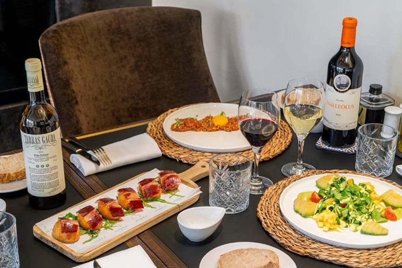 Une table à manger dressée avec des assiettes remplies de nourriture, des verres de vin et des bouteilles de vin.