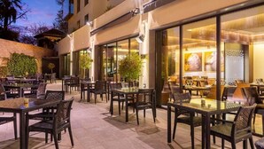 An outdoor dining area with tables and chairs, a brick wall, and a building with large windows.