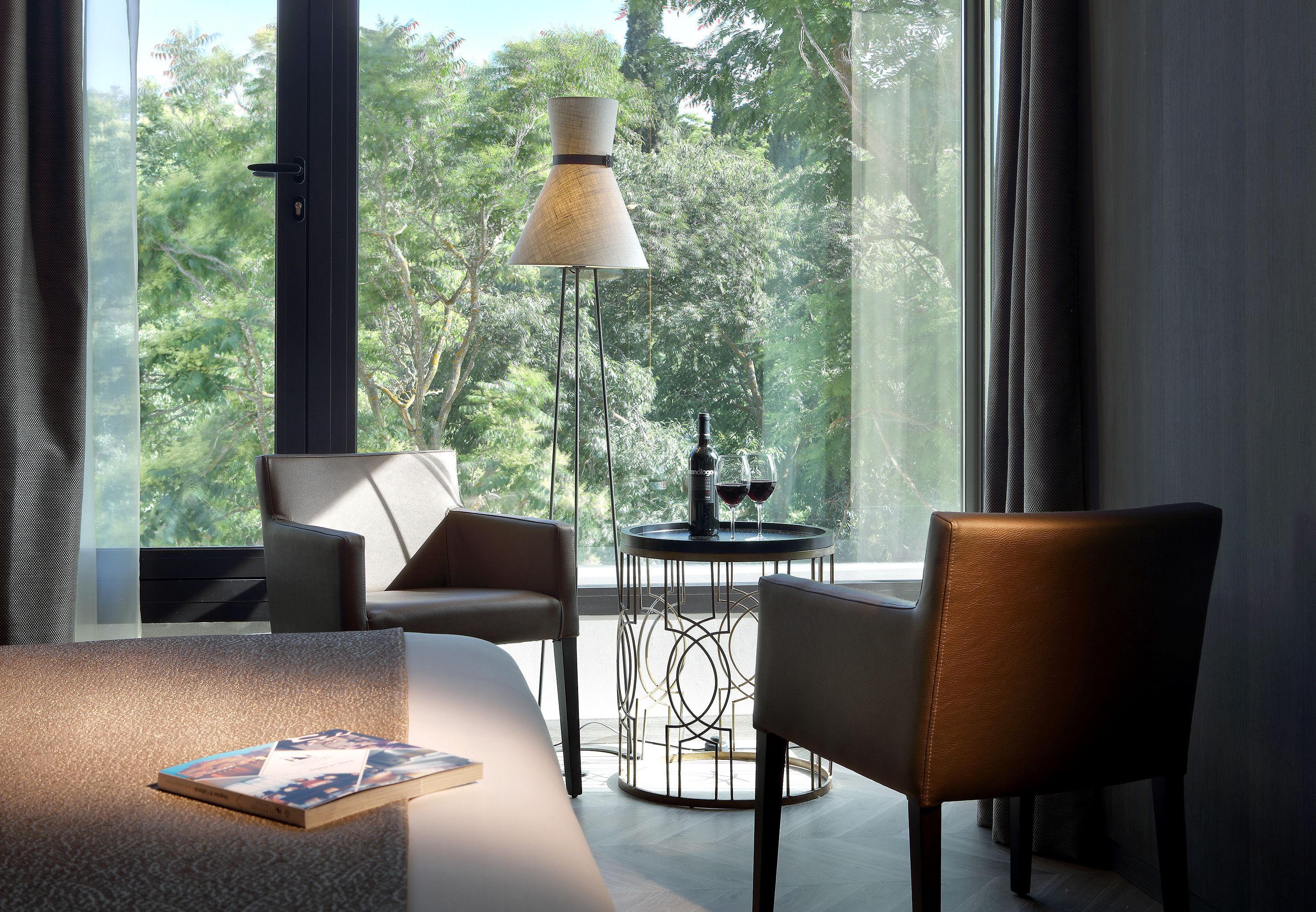 Ein modernes Zimmer mit einem großen Fenster, einem runden Tisch mit zwei Weingläsern und einer Stehlampe.