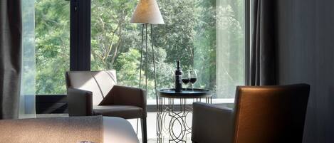 A modern room with a large window, a round table with two wine glasses, and a floor lamp.