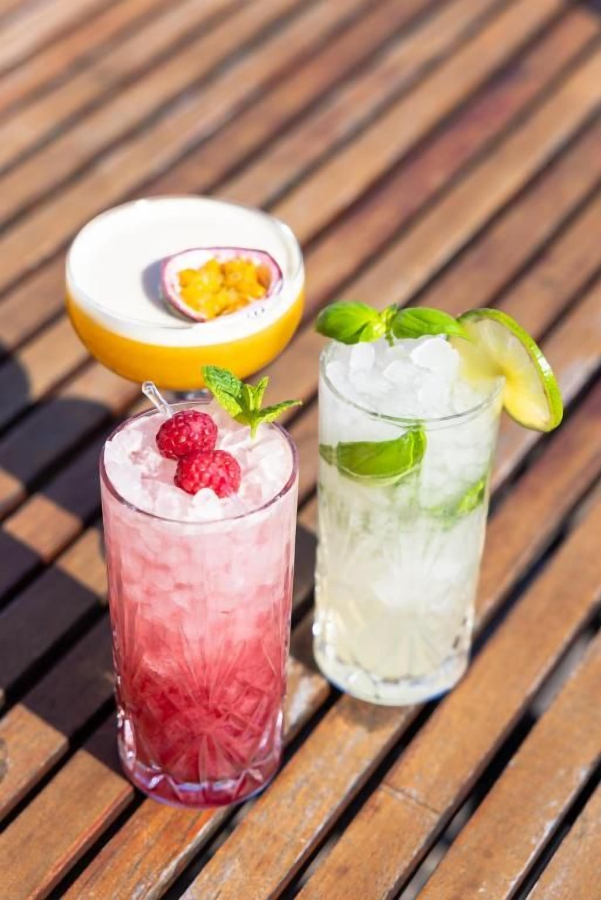 Two glasses of iced beverages with fruit garnishes on a wooden surface.