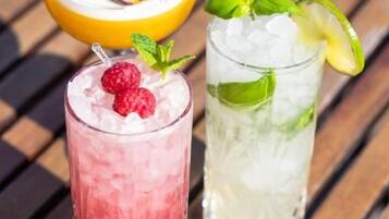 Two glasses of iced beverages with fruit garnishes on a wooden surface.