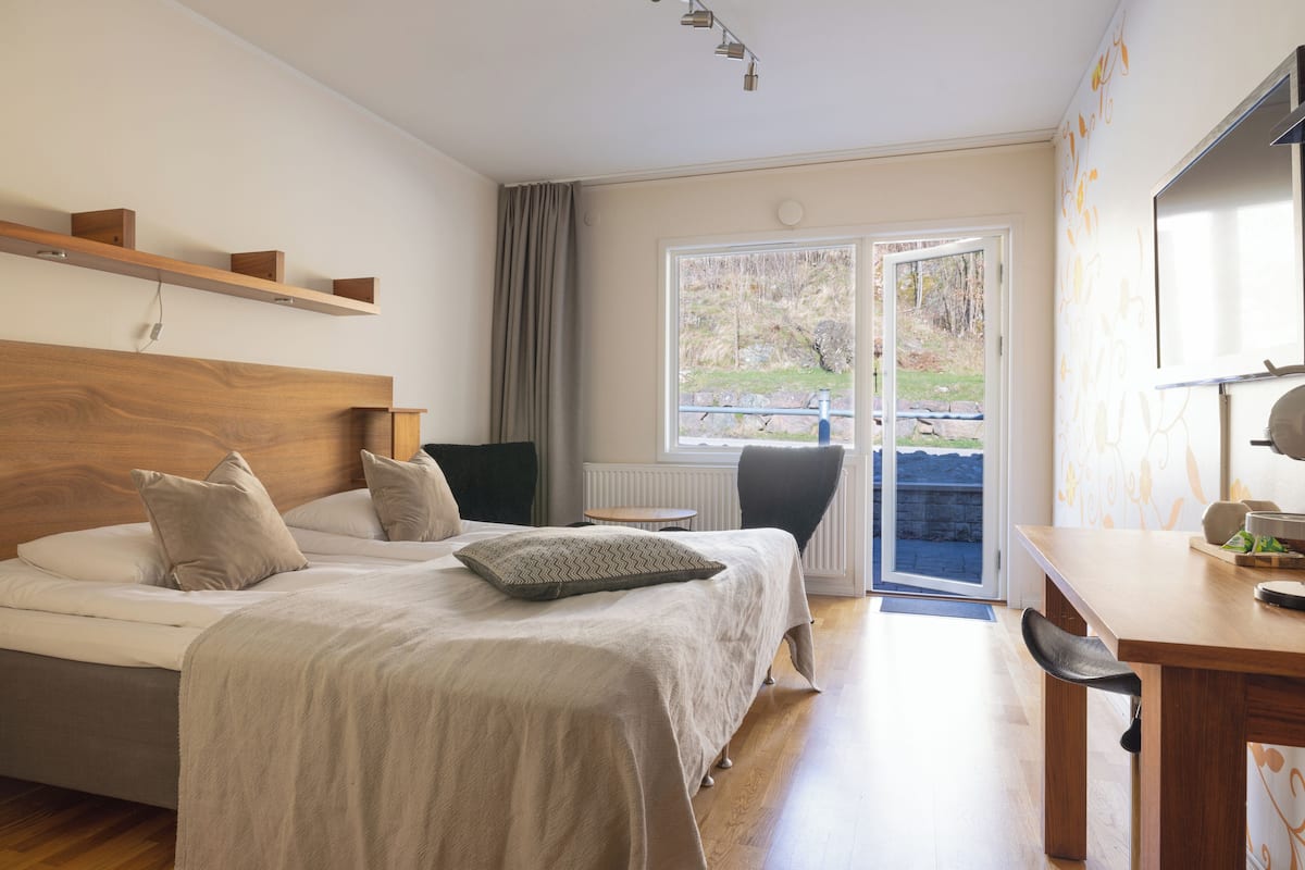 Un dormitorio con cabecera de madera, cama con ropa de cama color beige, una mesita y una silla.