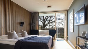 Un dormitorio moderno con una cama grande, un escritorio y vistas a un árbol a través de un ventanal.