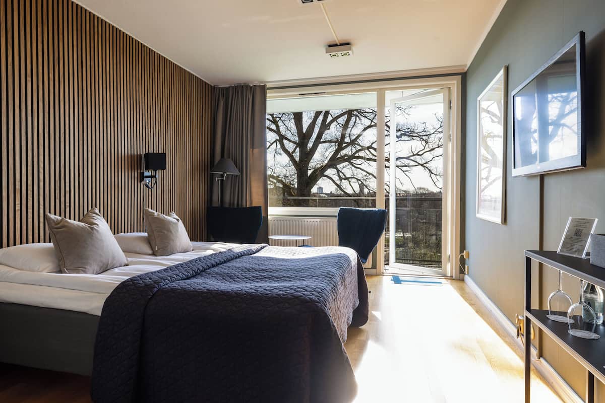 Un dormitorio moderno con una cama grande, un escritorio y vistas a un árbol a través de un ventanal.