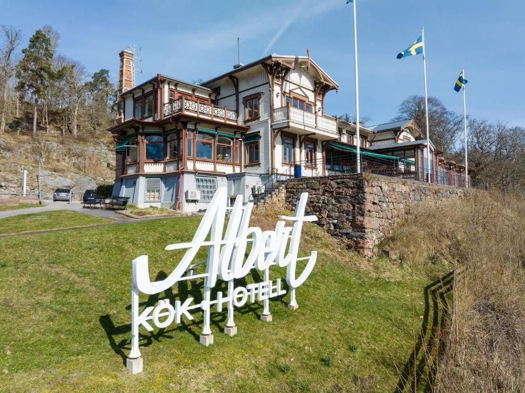 A two-story building with a balcony, a stone wall, and a sign reading 'Albert Kok Hotel'.