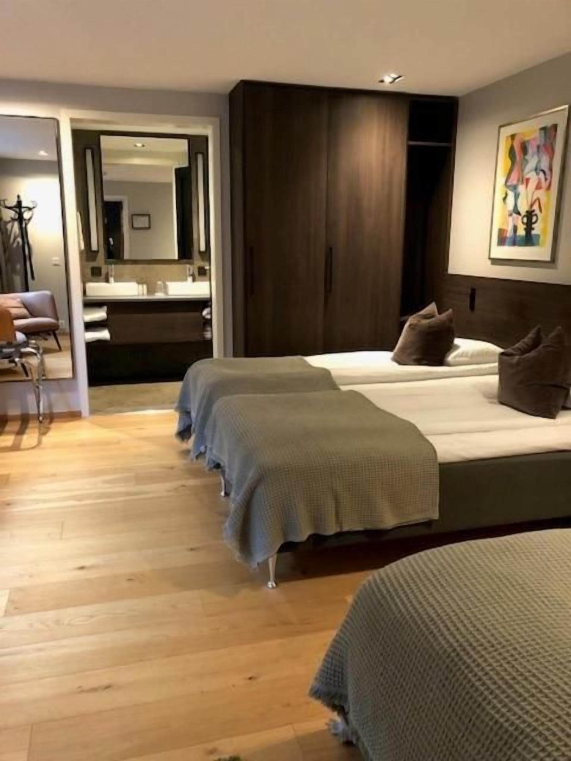 Una habitación de hotel con una cama grande, un sofá independiente, suelo de madera, un armario y un baño visible a través de una puerta abierta.