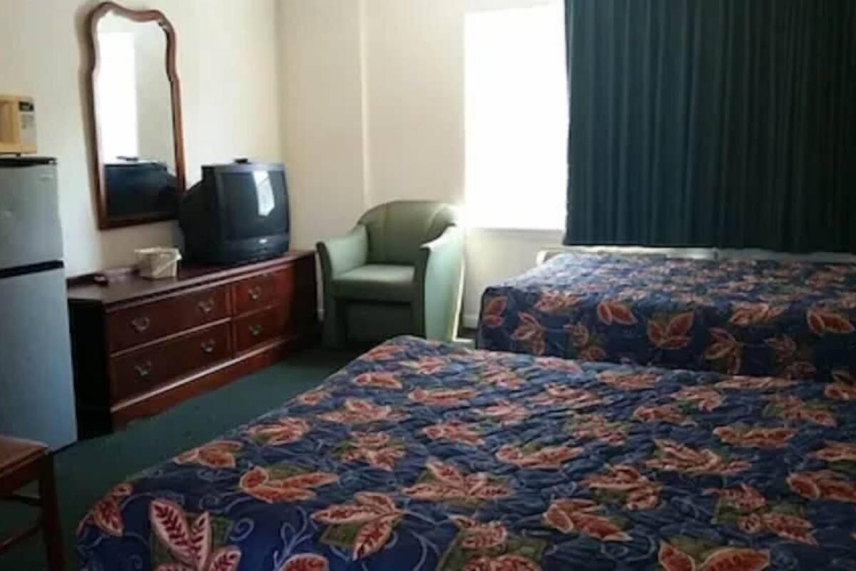 A hotel room with two beds, a dresser, a television, a microwave, and a chair.