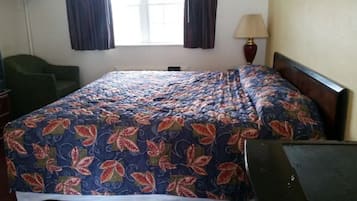 Een hotelkamer met een bed, een bureau, een stoel, een lamp en een raam met gordijnen.