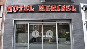 Et hotelskilt med navnet "HOTEL MERIBEL" og en stor glasklædt indgang.