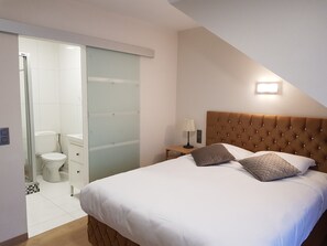 Un dormitorio con una cama grande, una mesita de noche, una lámpara y una puerta corredera que da a un baño.