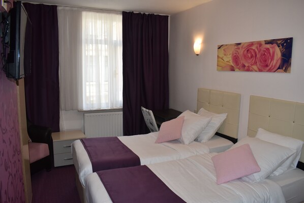 Habitación de hotel con dos camas, un escritorio, una silla y una ventana con cortinas.
