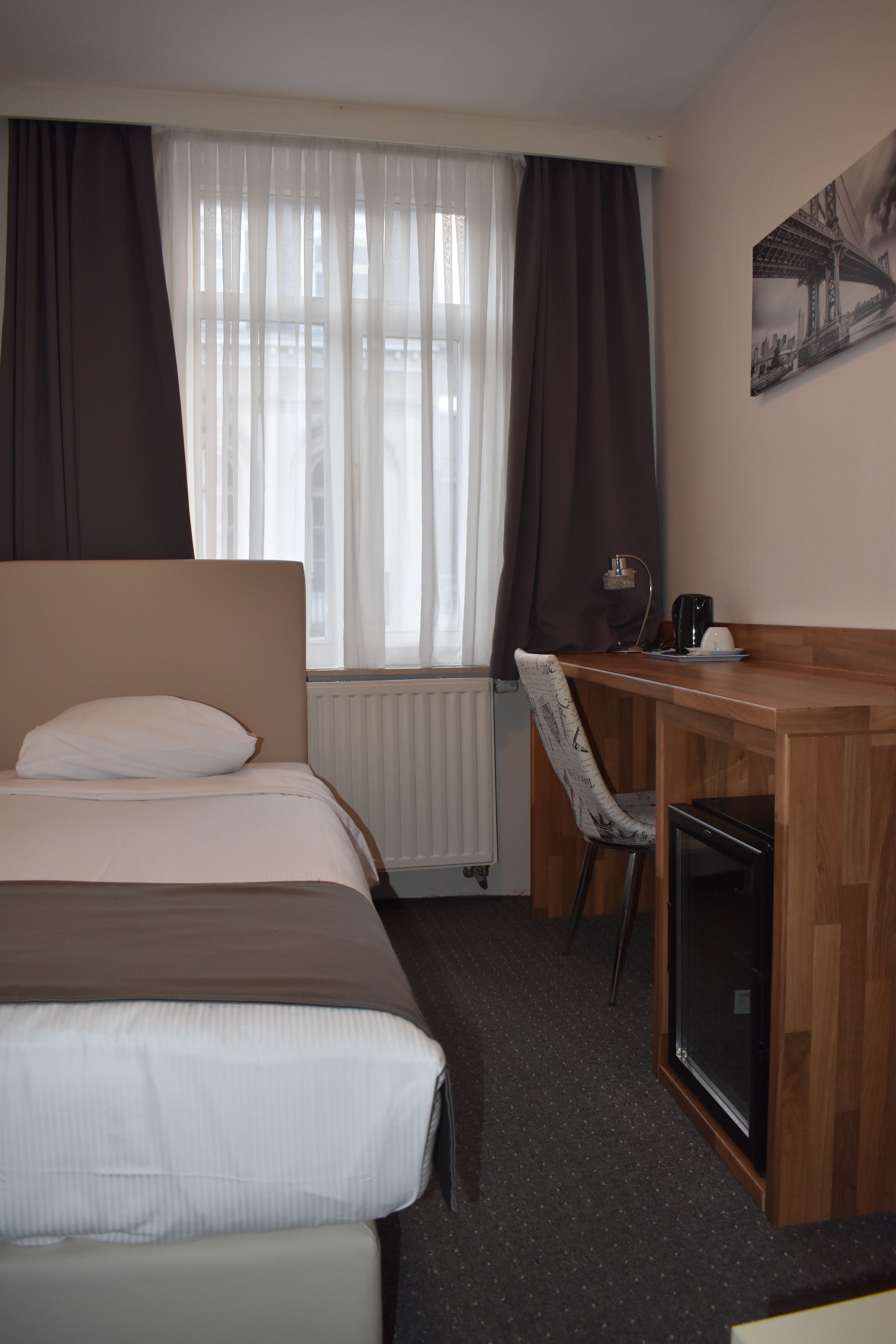 A hotel room with a bed, a desk, a chair, and a small refrigerator.