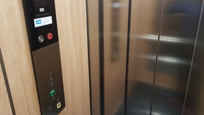 Betjeningspanel til elevator med digitalt display, kontaktoplysninger i nødstilfælde og et tastatur.