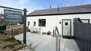 Schild für Heaps House, eine luxuriöse Ferienunterkunft mit Steinmauer, einer Tür und einer kleinen Terrasse mit Tisch und Stühlen.