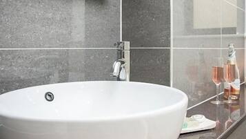 A bathroom with a white sink, a modern faucet, and a mirror above it. There are two glasses and a bottle on the countertop.