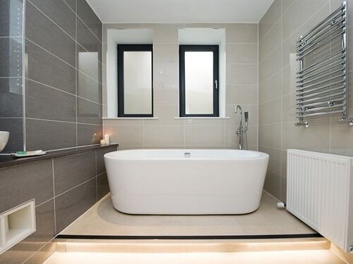 Ein modernes Badezimmer mit einer freistehenden Badewanne, zwei Spiegeln über dem Waschbecken und einem Handtuchhalter an der Wand.