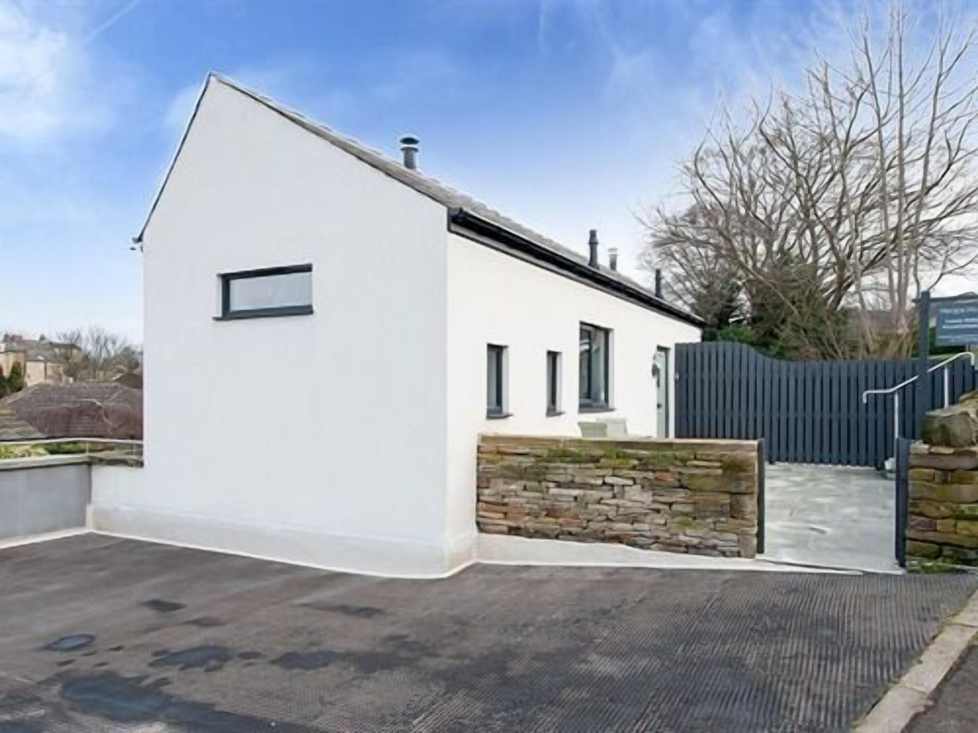A modern white building with a stone wall entrance, a gated driveway, and a clear sky.