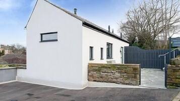 A modern white building with a stone wall entrance, a gated driveway, and a clear sky.