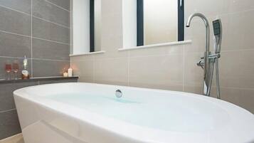 Un baño moderno con una bañera independiente, un cabezal de ducha manual y un espejo sobre la bañera.