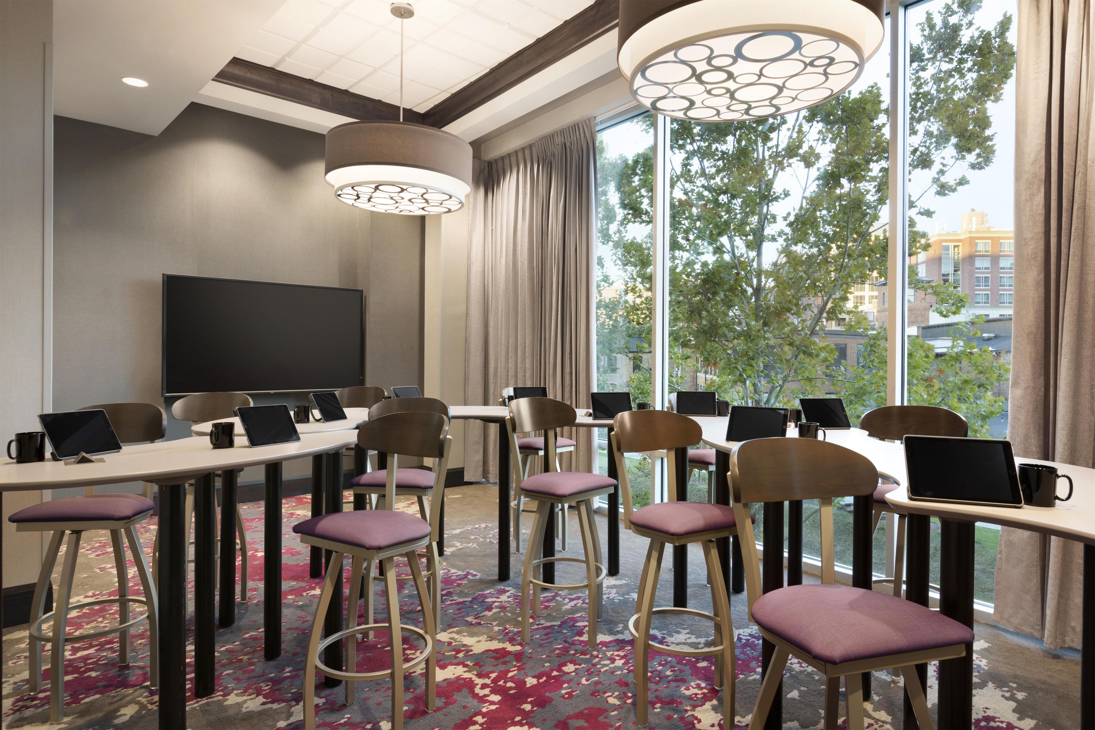 Une salle de conférence dotée de plusieurs tables, de chaises et d’ordinateurs portables, et équipée d’un grand écran et d’un système d’éclairage moderne.